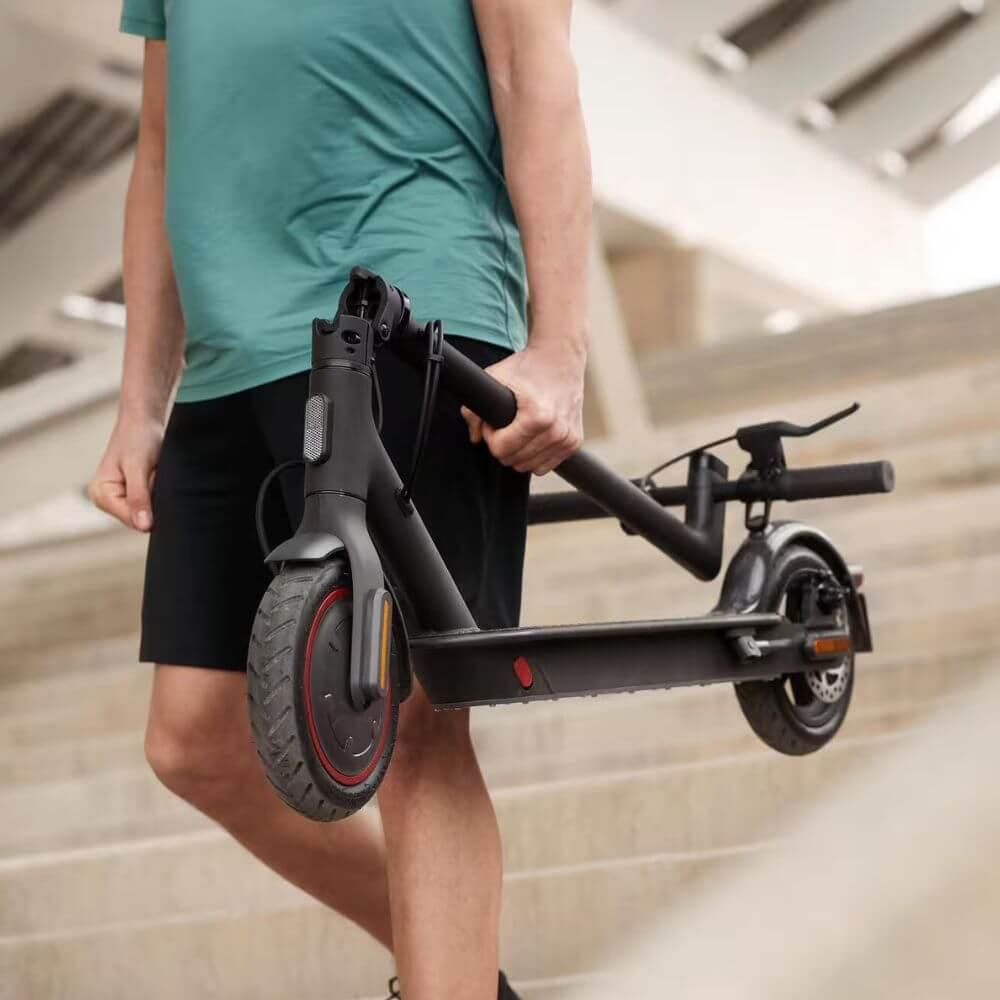 Unhomme en tshirt bleu qui porte sa trottinette électrique pliante