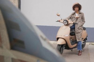 Femme assise sur un scooter électrique Brumaire 4700W beige à l’arrêt