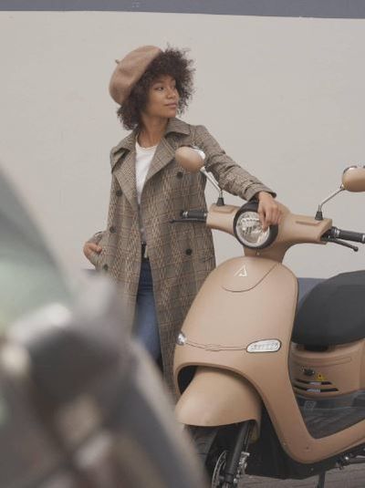 Jeune femme posant sa main gauche sur le guidon d’un scooter électrique Brumaire beige
