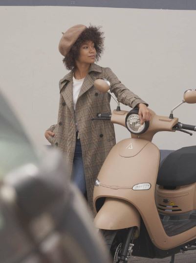 Jeune femme posant sa main gauche sur le guidon d’un scooter électrique Brumaire beige